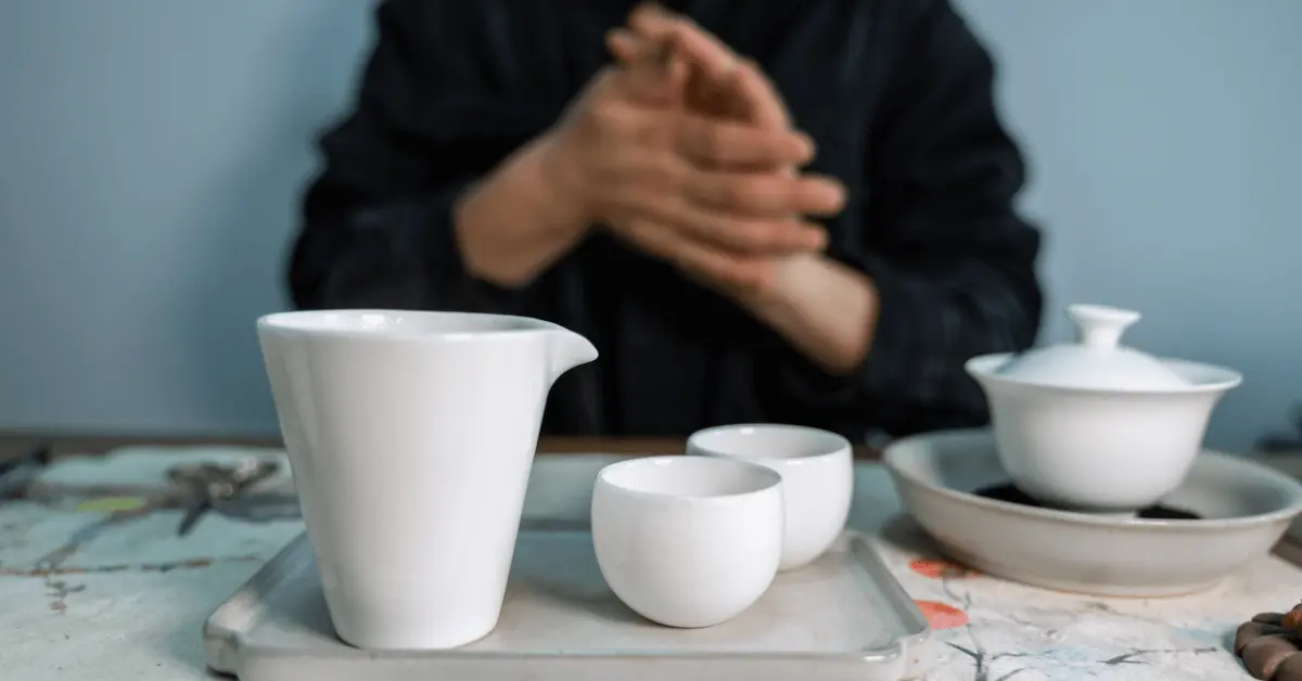 a person sitting at a table with a white tea set and a cup