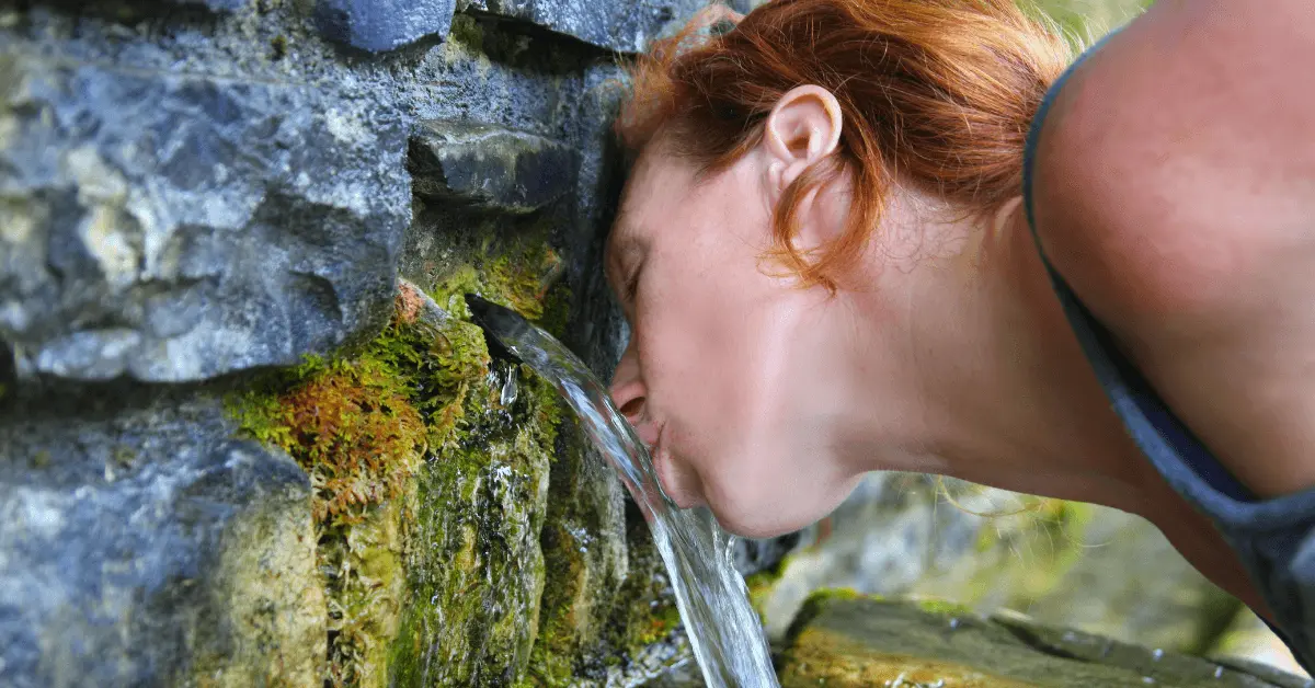 a woman drinking water from a spring